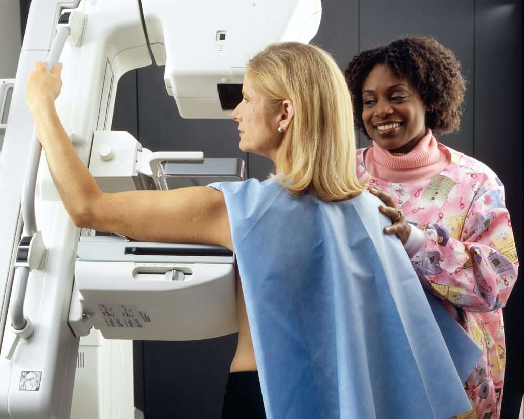 Mammography what to expect smiling woman standing near another woman beside mammogram machine