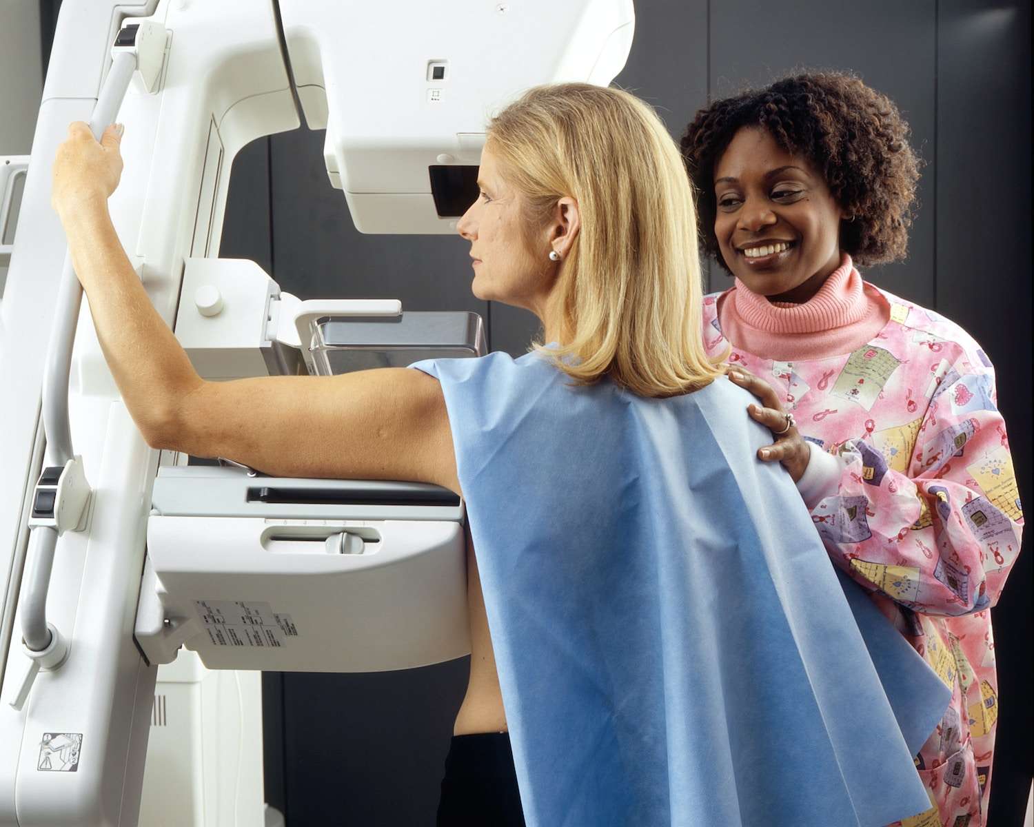 Mammography what to expect smiling woman standing near another woman beside mammogram machine