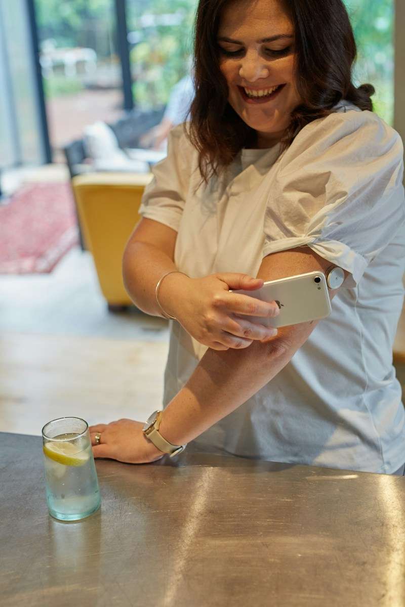 continuous glucose monitoring or CGM a woman sitting at a table holding a cell phone