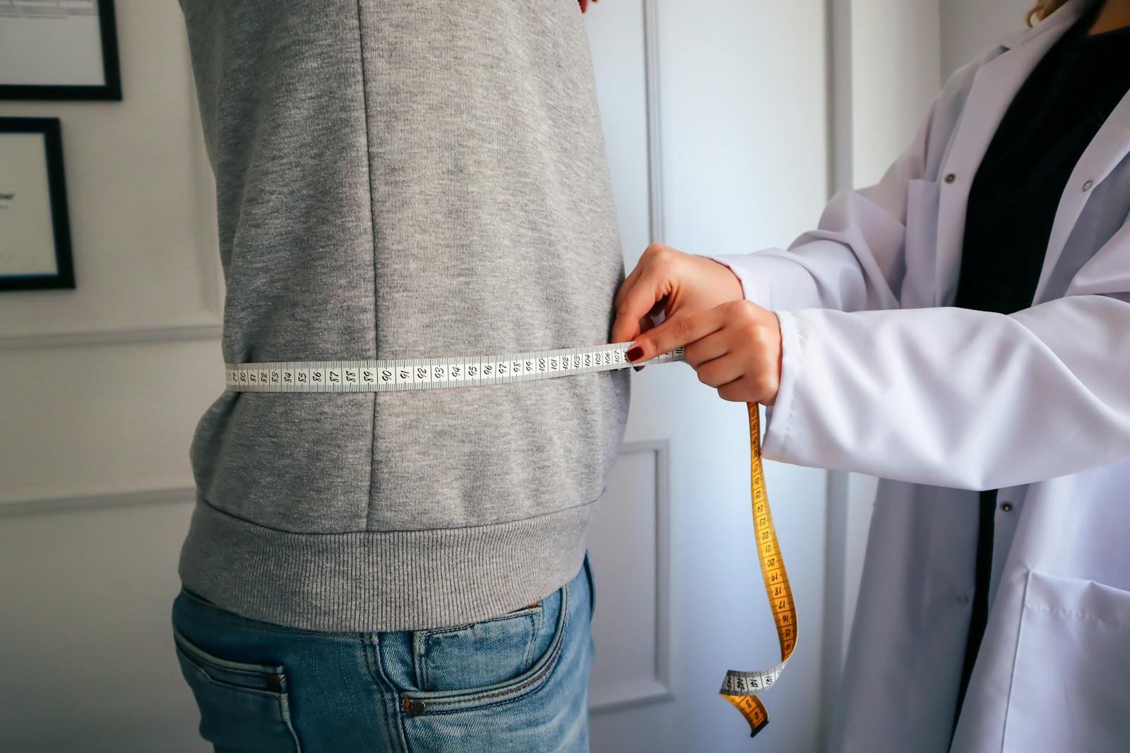 BMI or Body Mass Index A nutritionist measuring a patient's waist using a tape in a clinical setting.