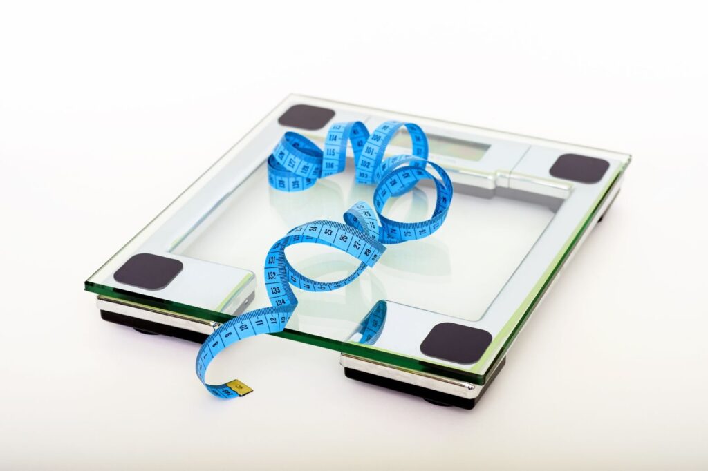 6 reasons why you are not losing weight A digital glass weighing scale with a blue measuring tape, symbolizing weight management.